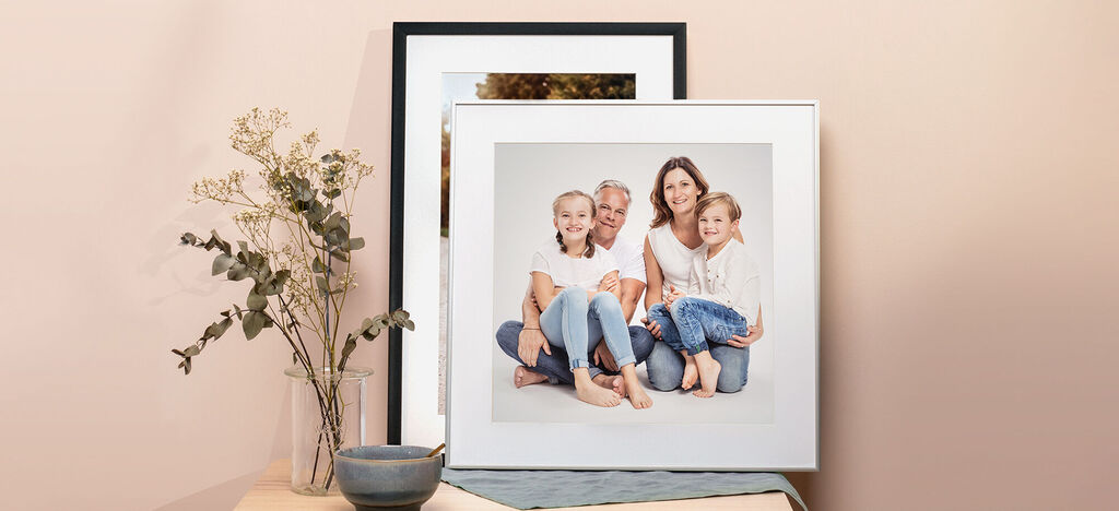 Famiglia posa felicemente in una cornice, con uno sfondo di composizione di piante.