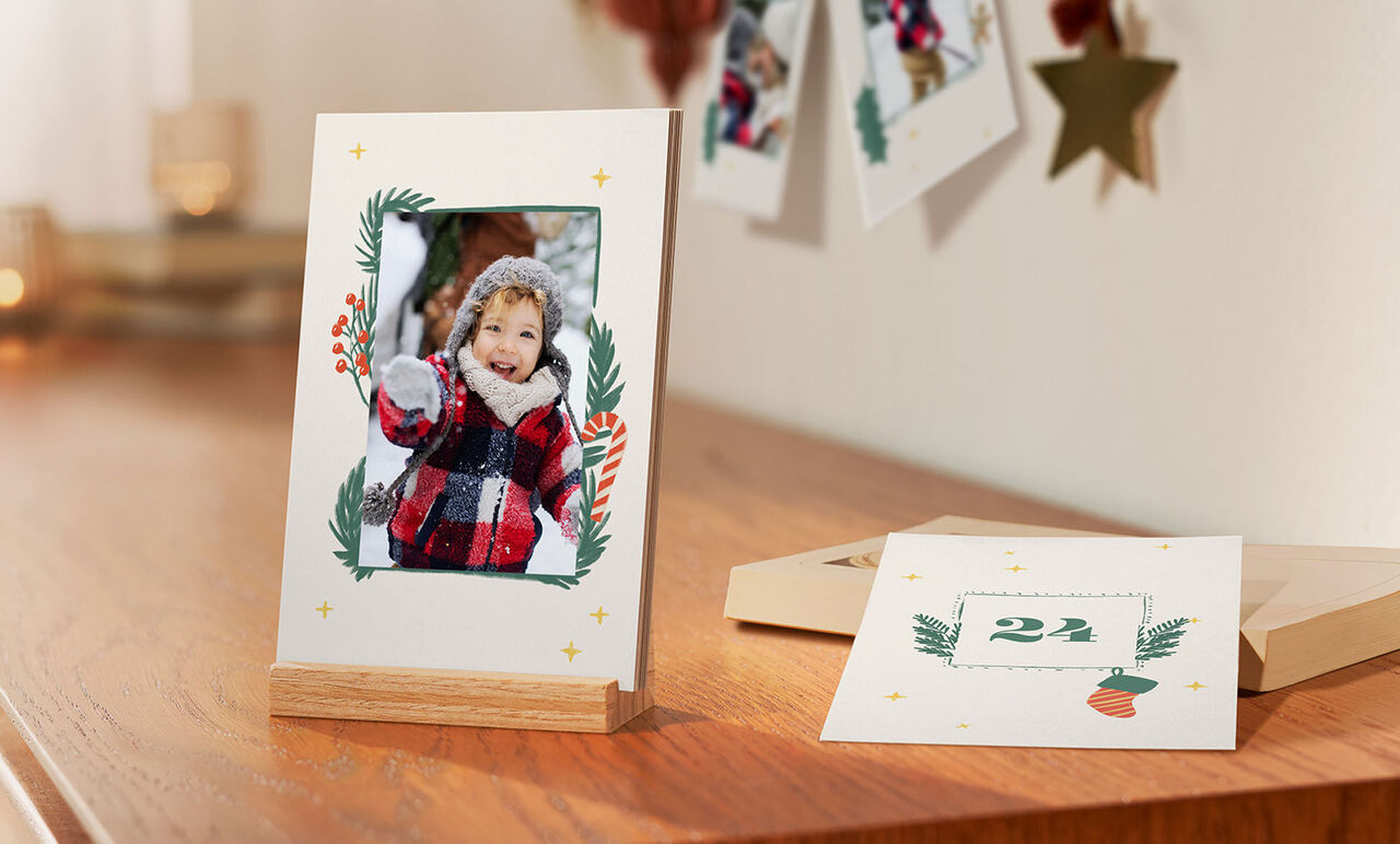 Un tavolo decorato con amore con una cornice che mostra un bambino in maglione rosso e bianco, circondato da decorazioni festive. Accanto c'è una carta con il numero 24.