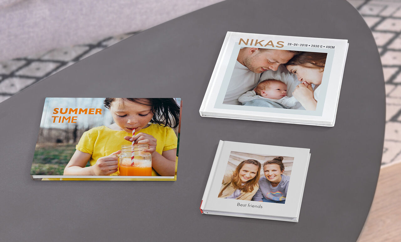 Tre bellissimi fotolibri su un tavolo, uno intitolato 'SUMMER TIME', un altro 'NIKAS', e il terzo 'Best Family'.