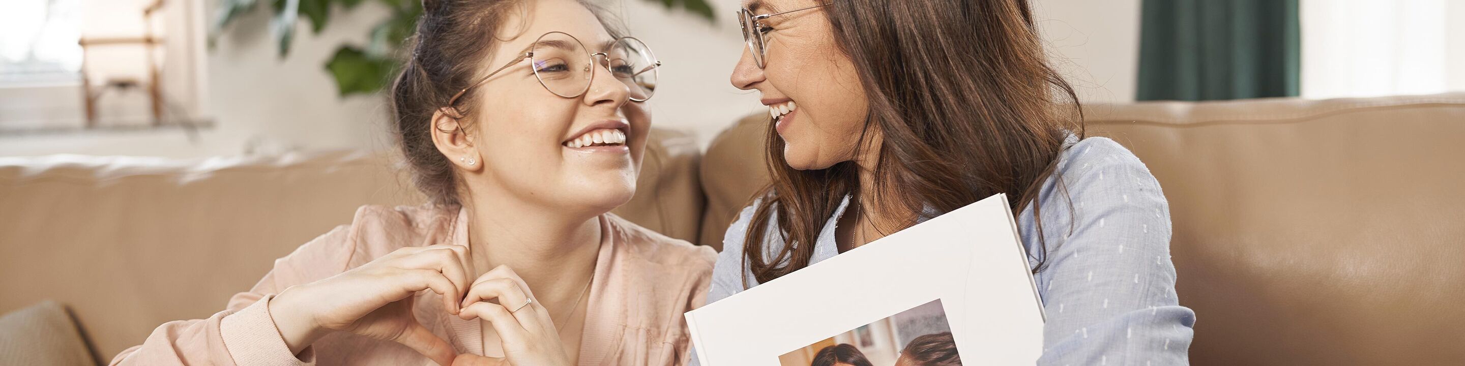 Due persone sedute su un divano con un album fotografico. Sorridono e mostrano un gesto affettuoso.