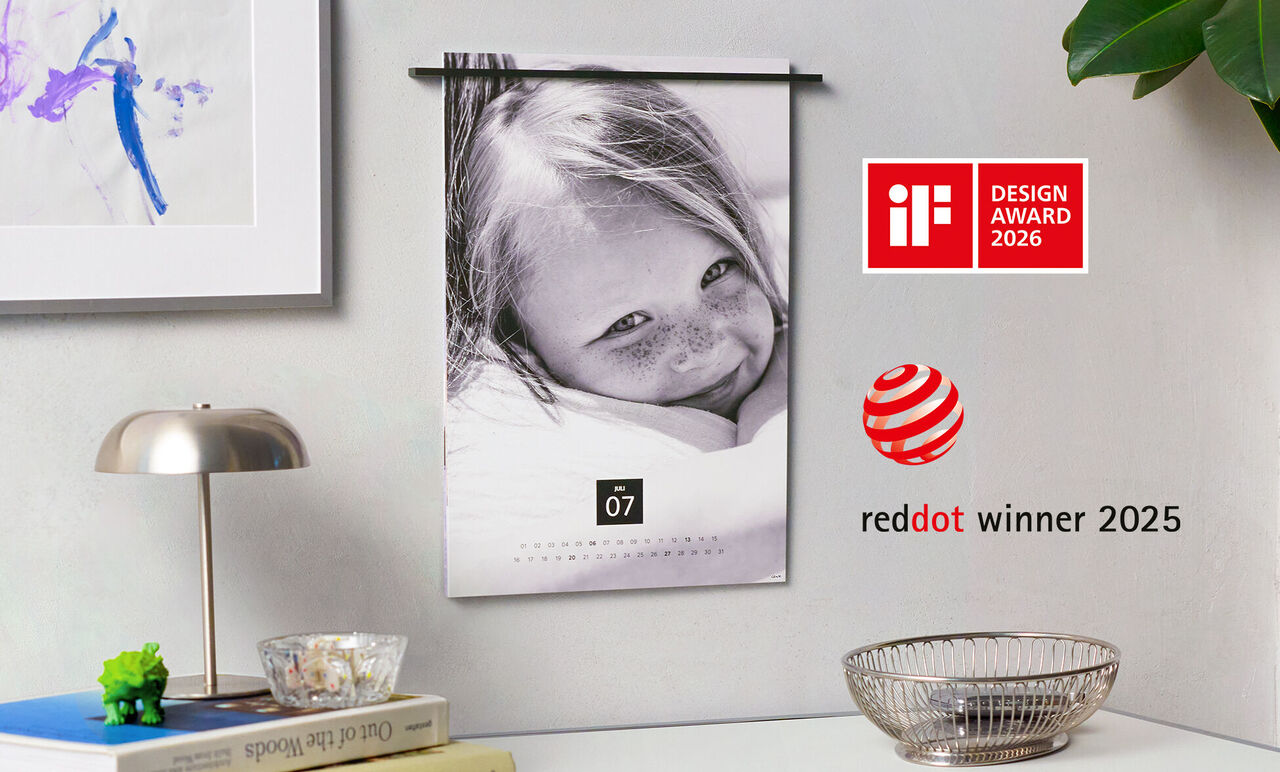 Calendario da parete con un bambino sorridente e uno sfondo bellissimo. Mostra il mese di luglio con il logo red dot Design Award.
