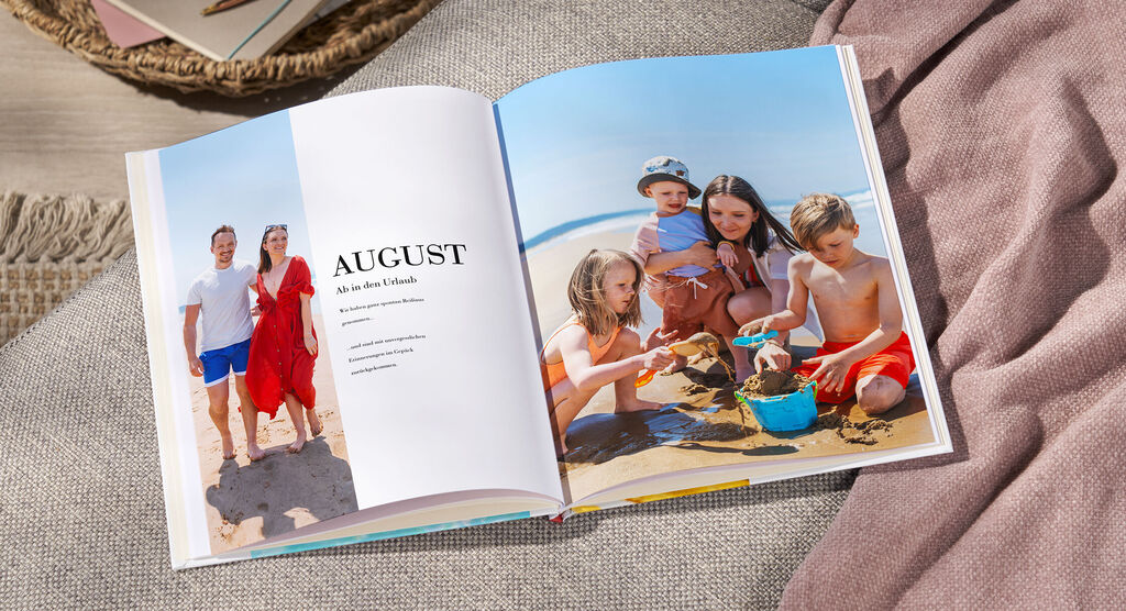 Una pagina aperta di un fotolibro mostra una vacanza al mare in agosto. Bambini giocano nella sabbia con formine.