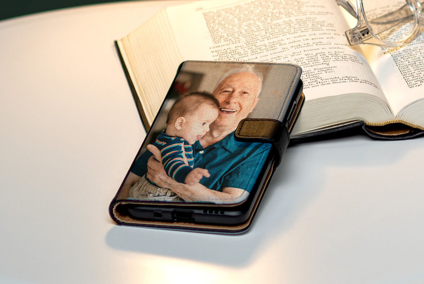 Una custodia per smartphone con l'immagine di un bambino e una persona anziana, accanto a un libro aperto