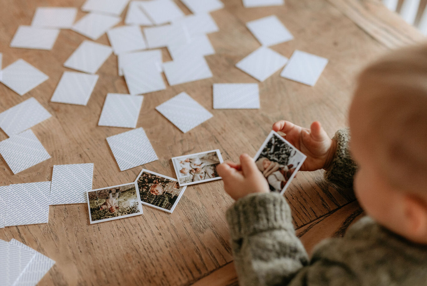 Bambino gioca con carte fotografiche su un tavolo in legno.