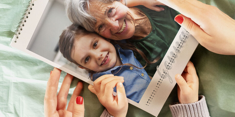 Due mani tengono un fotolibro con la foto sorridente di una donna anziana e un bambino.