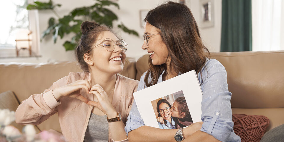 Due donne sedute su un divano mostrano un fotolibro con una foto insieme.