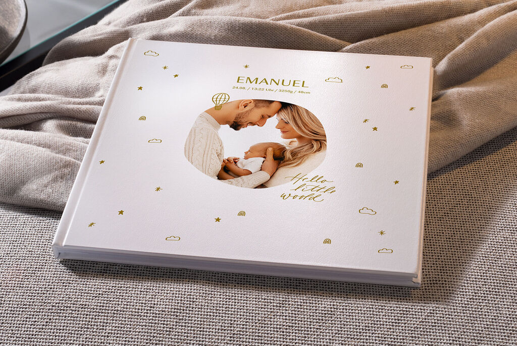 Un fotolibro CEWE amorevolmente creato dal nome Emanuel. La copertina mostra una coppia felice con un bambino tra stelle e nuvole dorate.