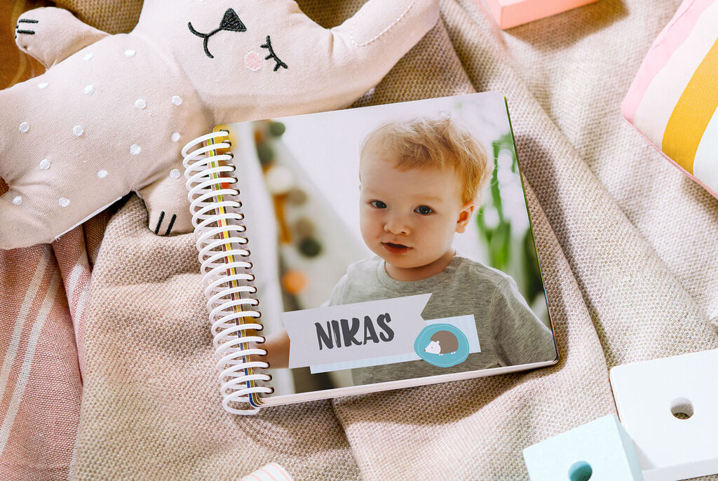 Un fotolibro con il nome Niklas in copertina, decorato con figure colorate e un peluche sullo sfondo.