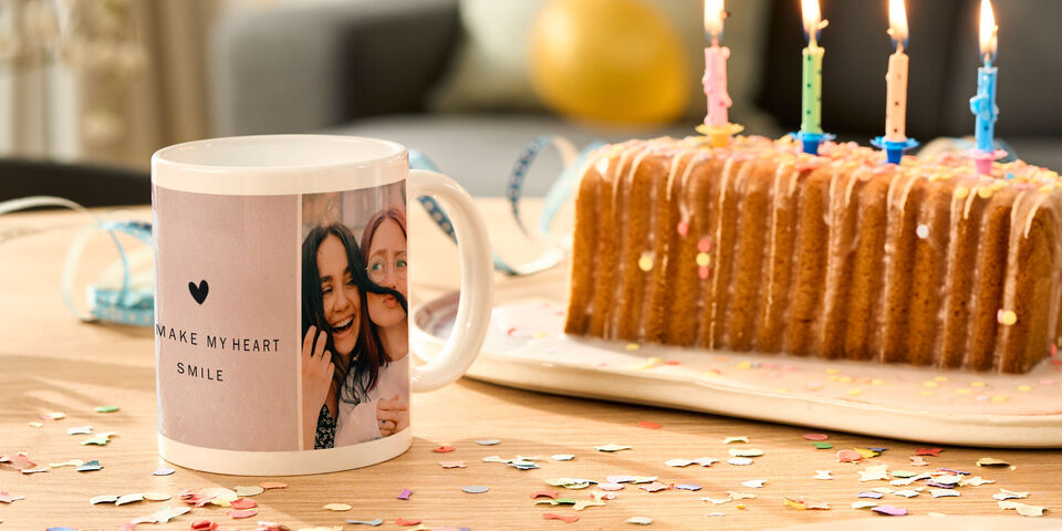 Una tazza con foto e testo personale accanto a una torta colorata con candele.