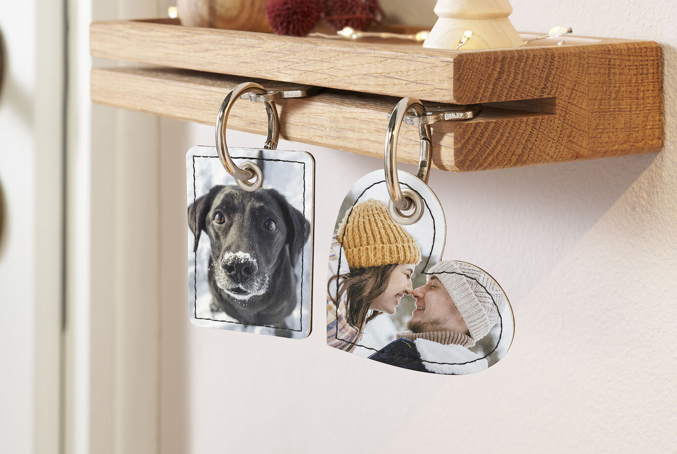 Due portachiavi personalizzati appesi a una tavola di legno. Uno mostra un cane, l'altro una persona con un cappello.